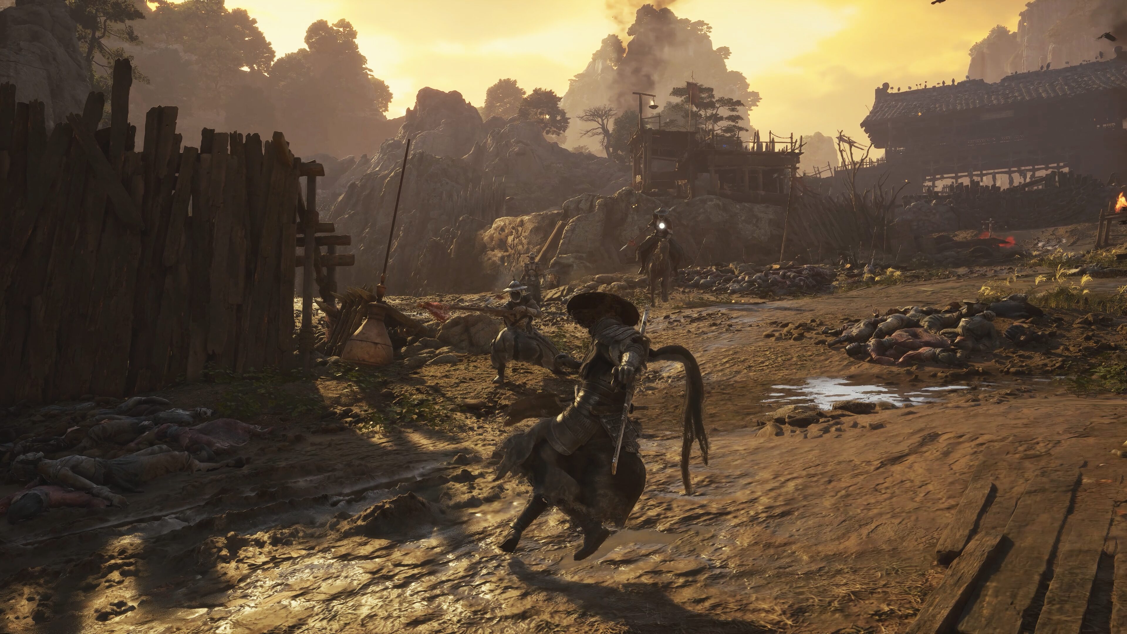 A swordsman standing on a dirt road at dusk between a wooden fence and a tiled hall, with a fallen body in the foreground.